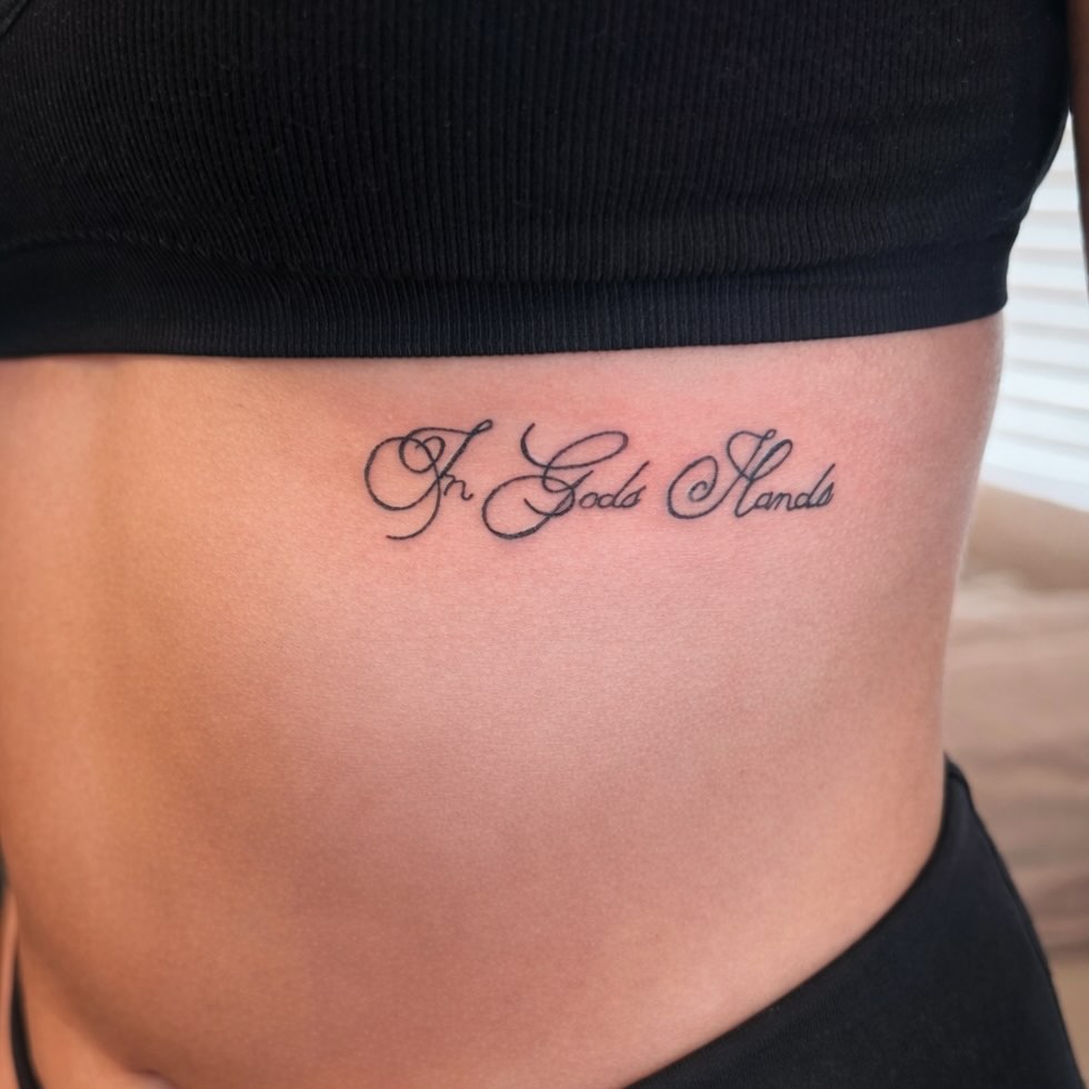 In God's Hands lettering script tattoo on the ribs by Victoria Cooper