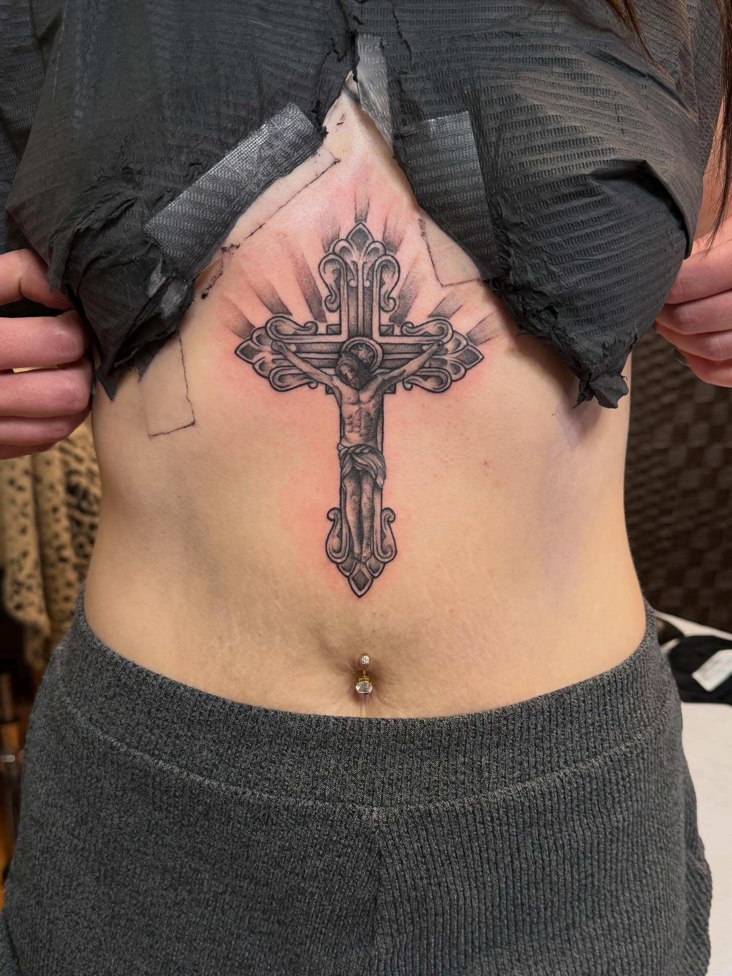 Cross with crucifixion scene black and grey tattoo on the torso by Madilynn Klassen
