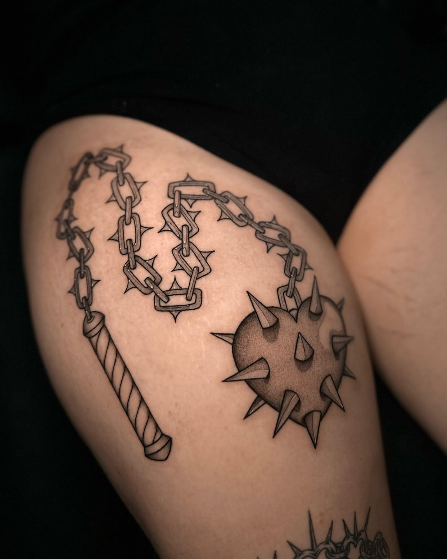 Spiked ball and chain black and grey tattoo on the thigh by Frida Tattooista