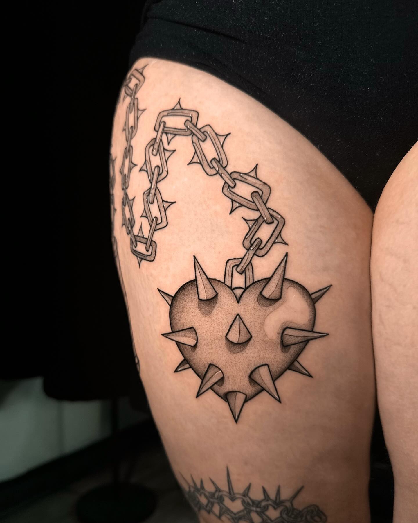 Spiked heart black and grey tattoo on the thigh by Frida Tattooista