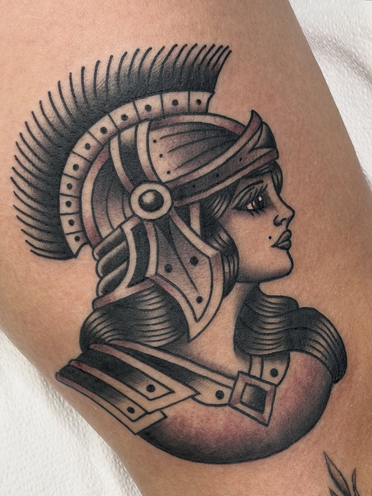 Female warrior helmet black and grey tattoo on the thigh by Cory Craft