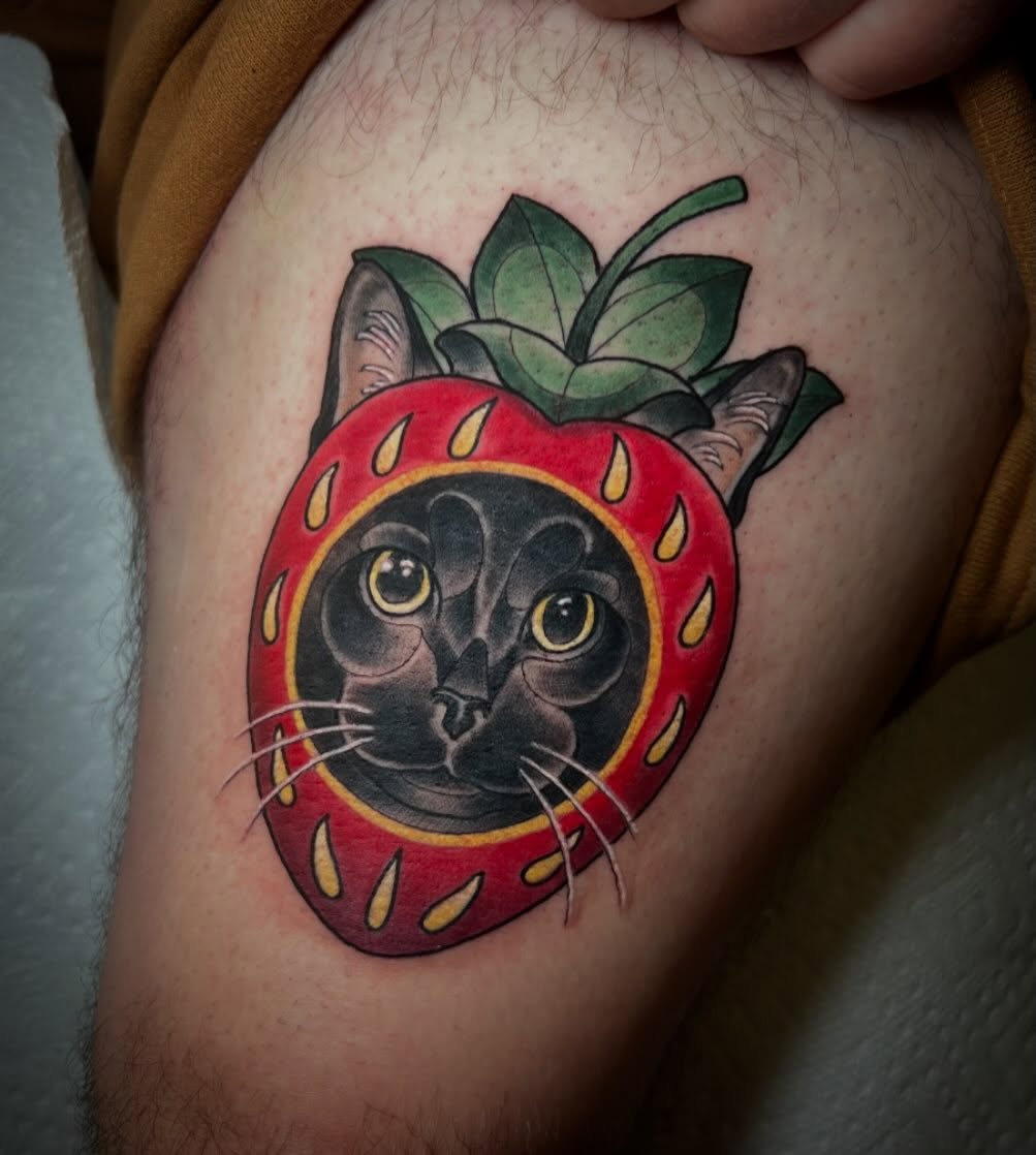 Cat in strawberry realism tattoo on the thigh by Katie Ann Tattoos
