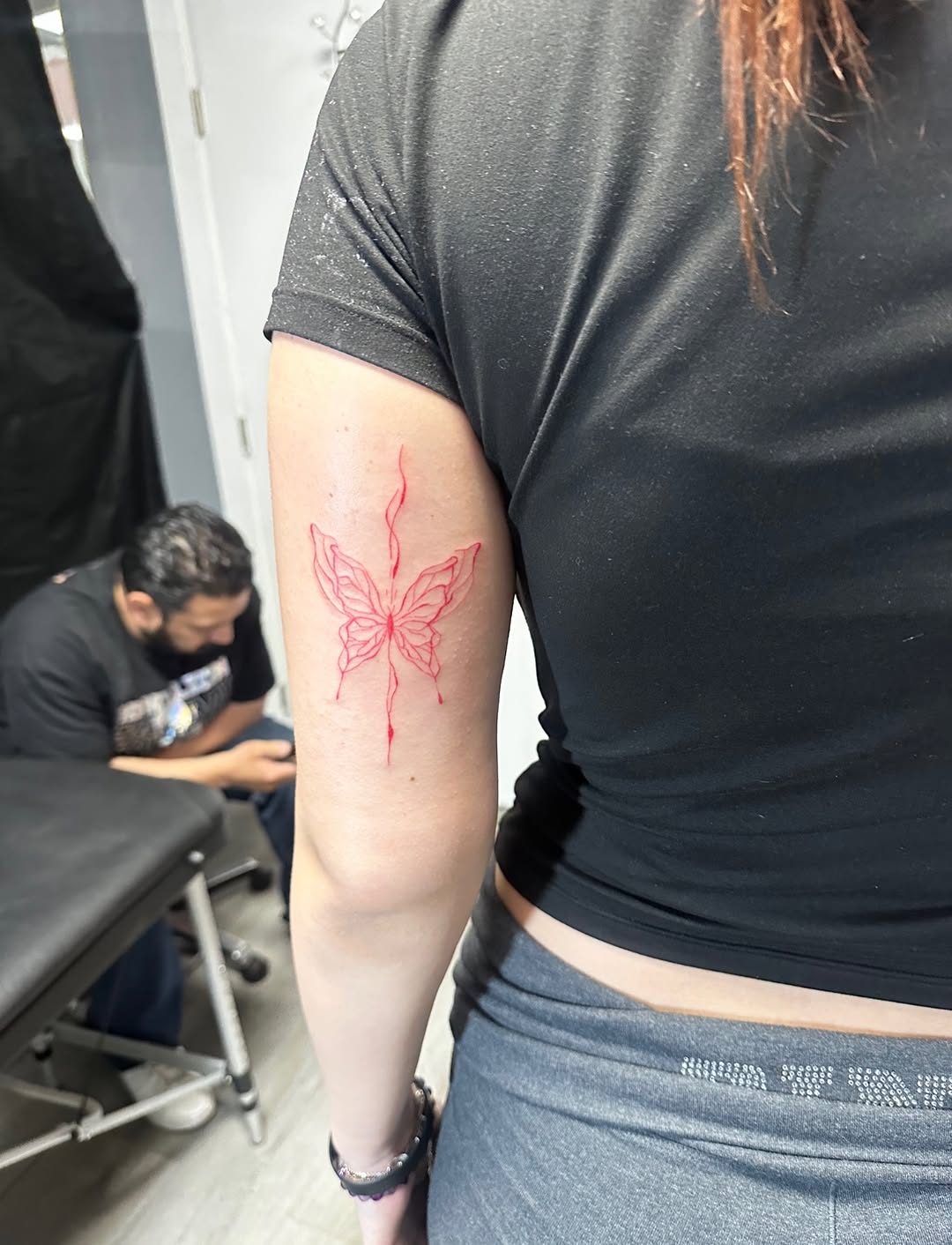 Red butterfly outline fine line tattoo on the forearm by Lupita Ink