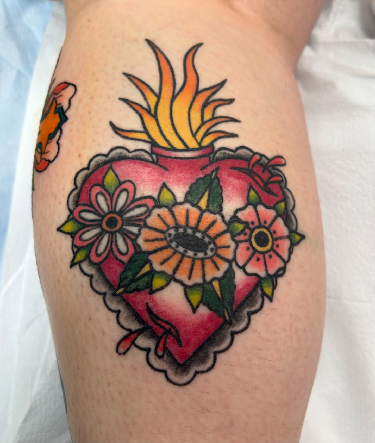 Heart with flames and flowers American traditional tattoo on the thigh by Courtney