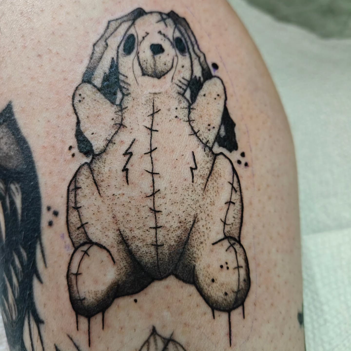 Stitch teddy bear black and grey tattoo on the upper arm by Meg
