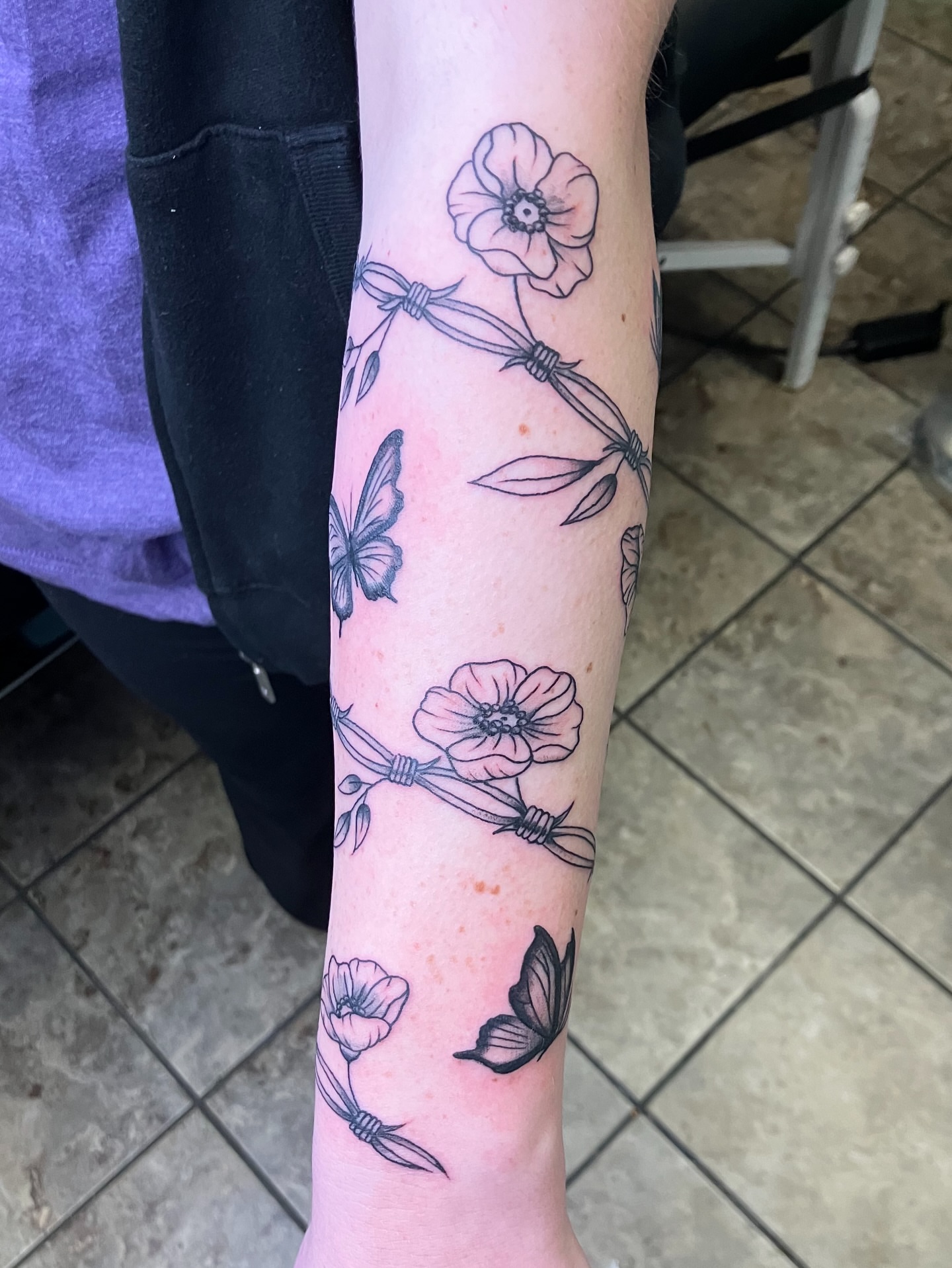 Barbed wire and flowers black and grey tattoo on the forearm by maddie mcghee, Memphis, Tennessee