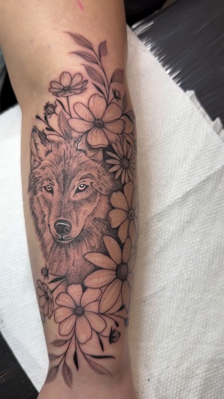 Wolf head surrounded by daisies realism tattoo on the forearm by WhoisLaineyTattoos