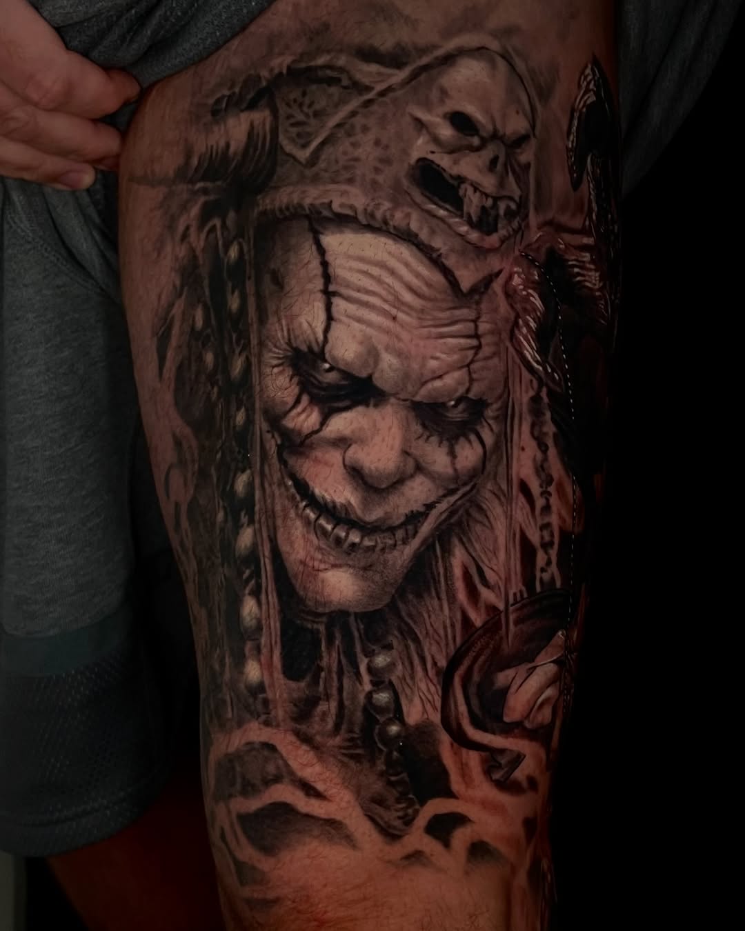 Creepy clown with skull headdress realism tattoo on the thigh by Tattoo Artist