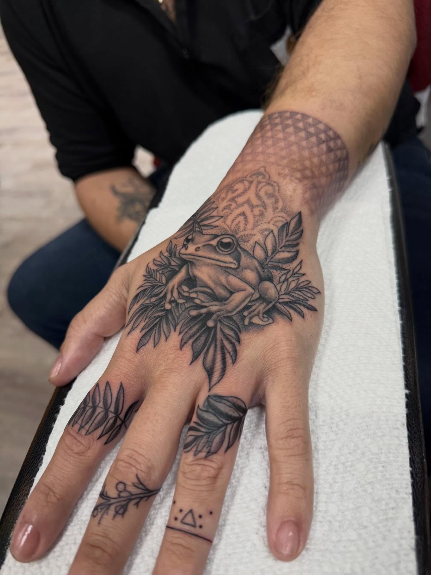 Frog and leaves black and grey tattoo on the hand by Diana Guillette