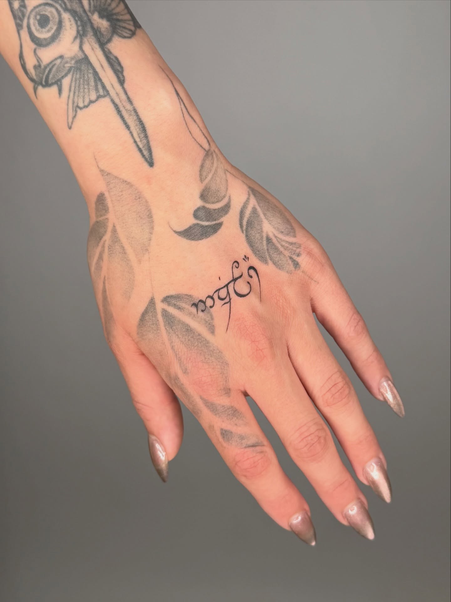 Leaf and script dotwork tattoo on the hand by Jerm Lewis