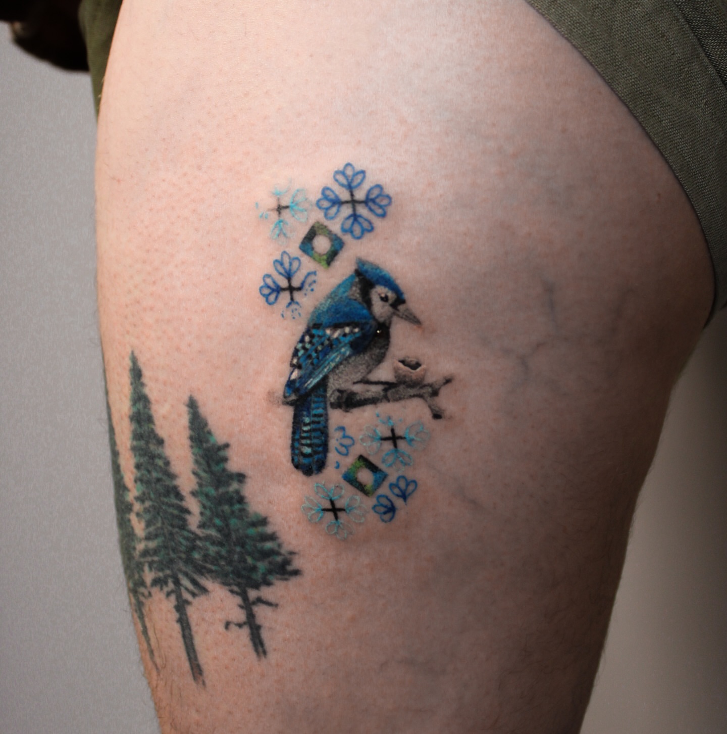 Blue jay and snowflakes realism tattoo on the thigh by Micah Light (color micro realism, Los Angeles, California