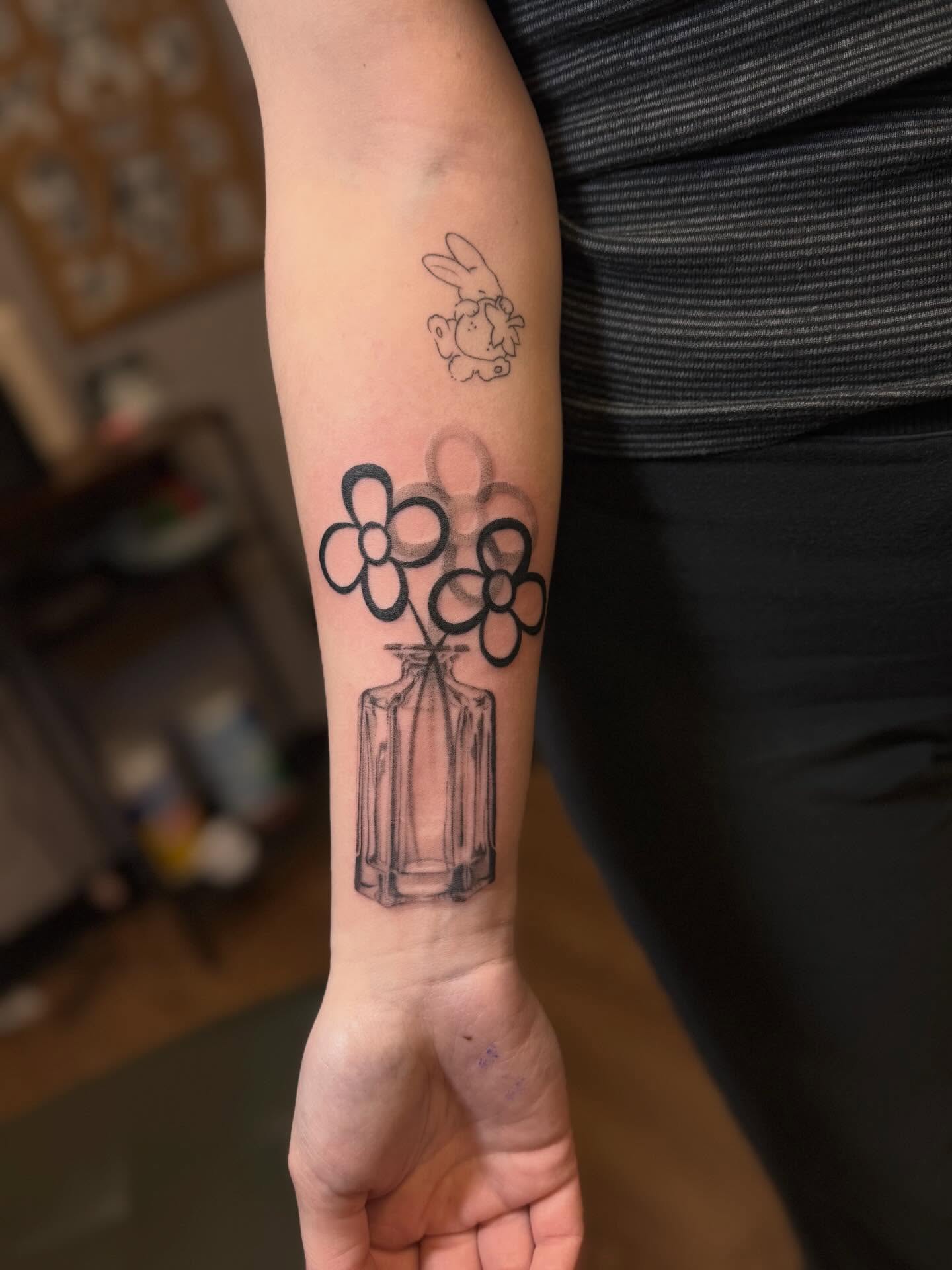 Bottle with flowers black and grey tattoo on the forearm by Anna
