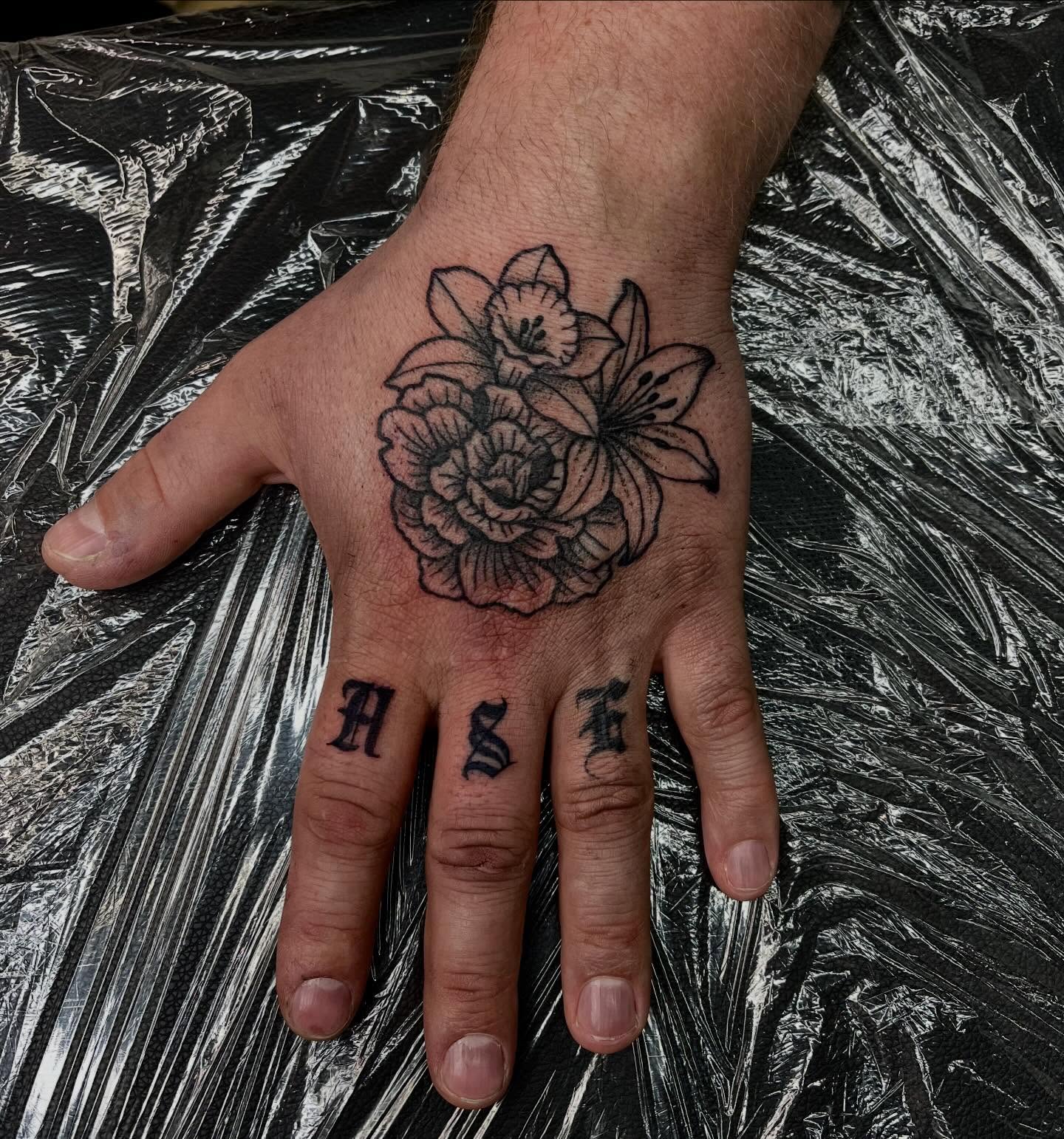 Floral arrangement black and grey tattoo on the hand by Mason McCubbin