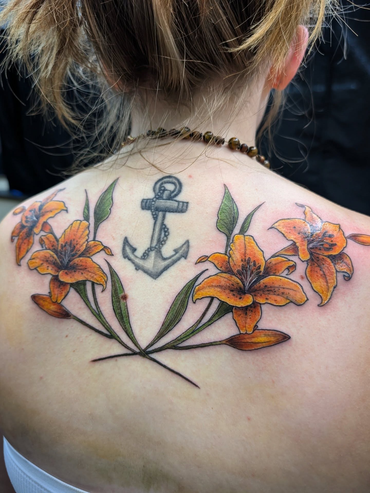 Lilies and anchor black and grey tattoo on the back by Katherine