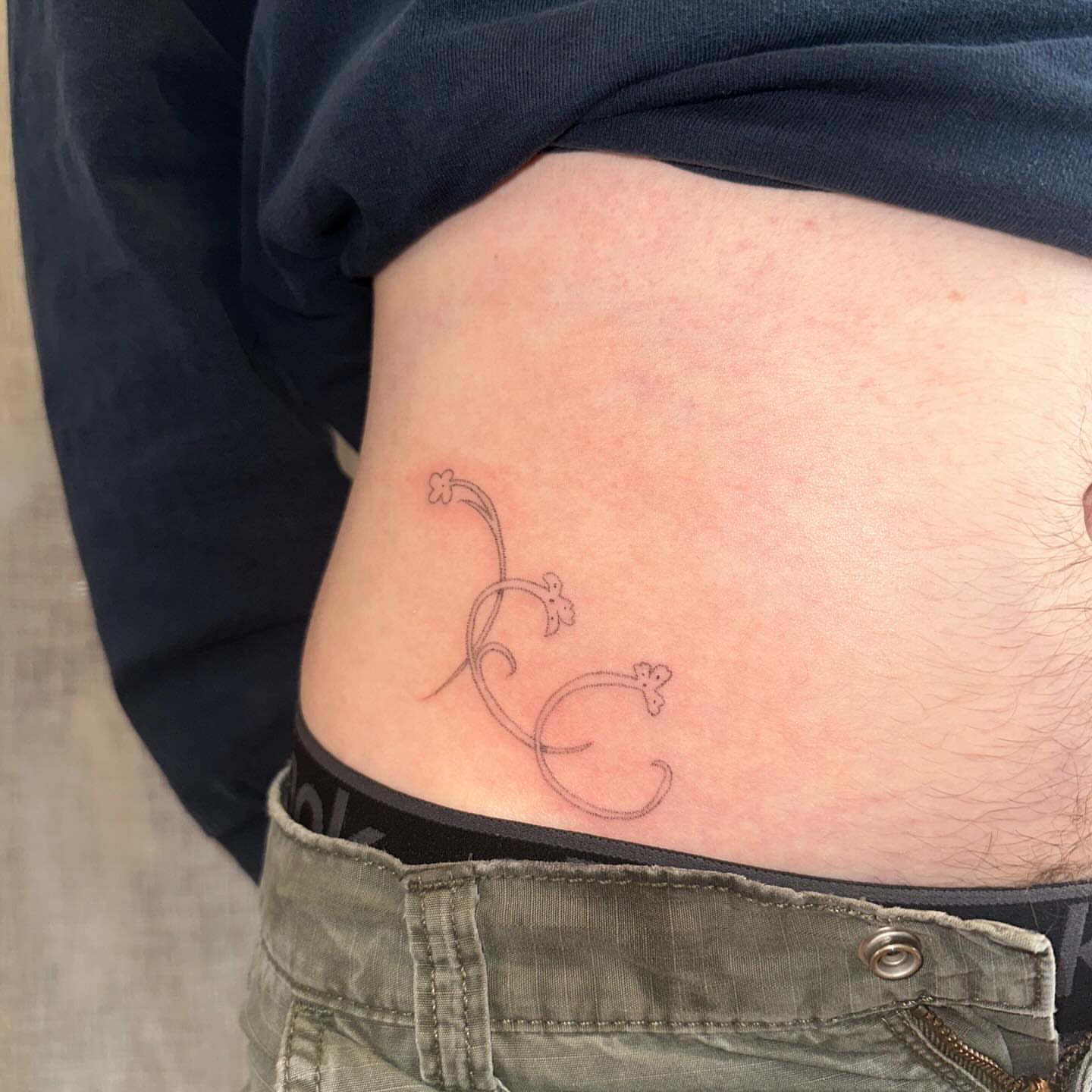Twisted floral design fine line tattoo on the torso by kate