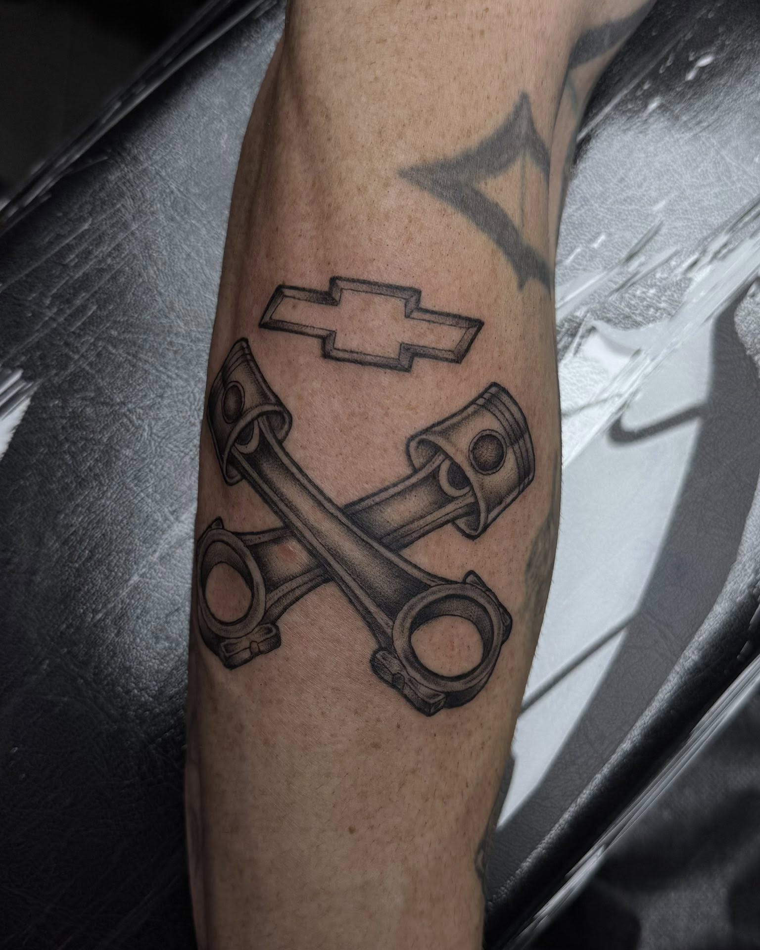 Chevrolet logo with crossed pistons black and grey tattoo on the forearm by Madison Jasso