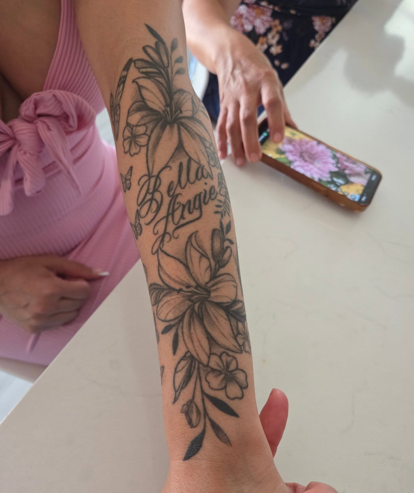 Floral arrangement with names black and grey tattoo on the forearm by Yvette Cebreros