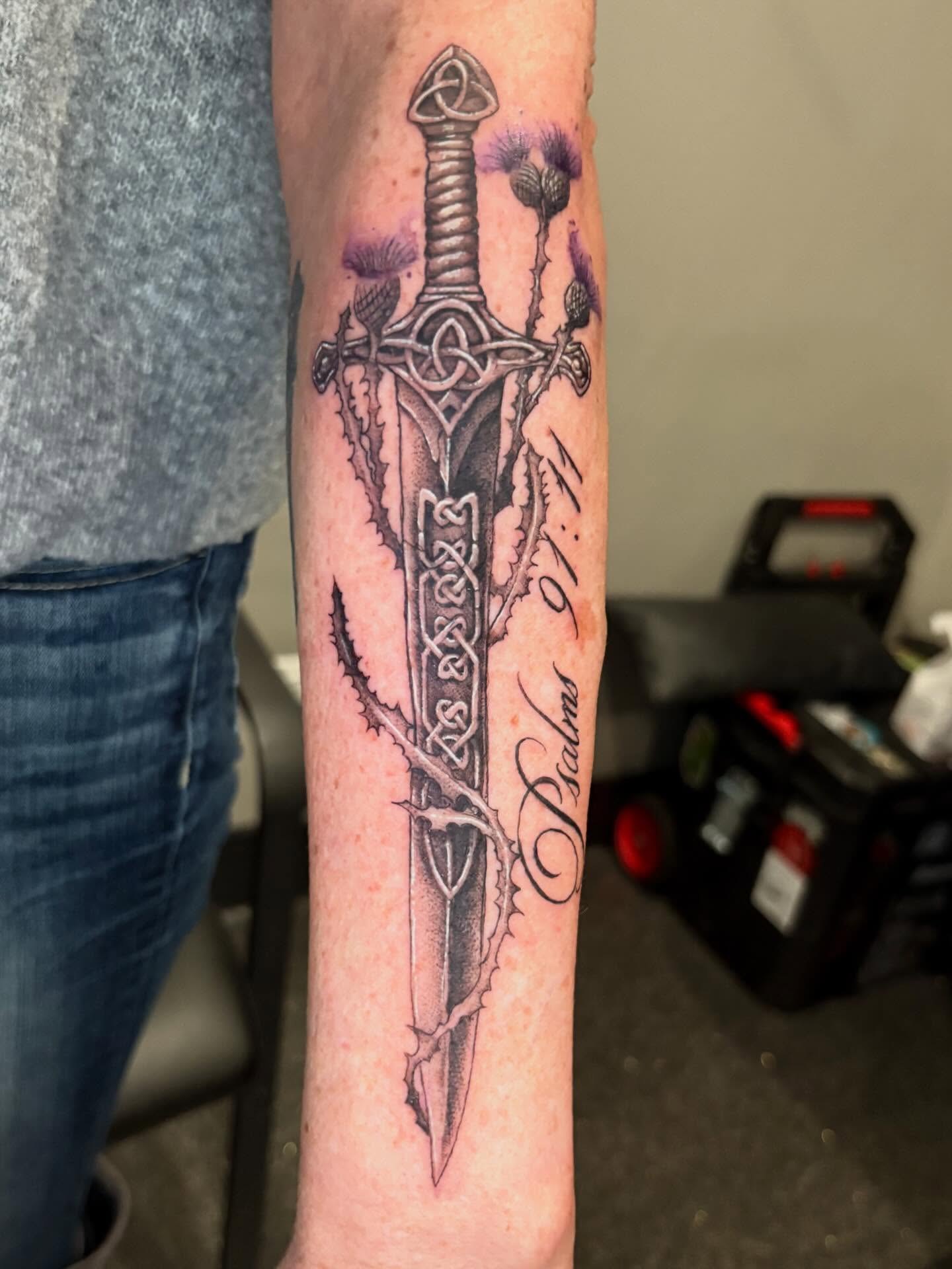 Sword and thistle black and grey tattoo on the forearm by Eddie Wolfe