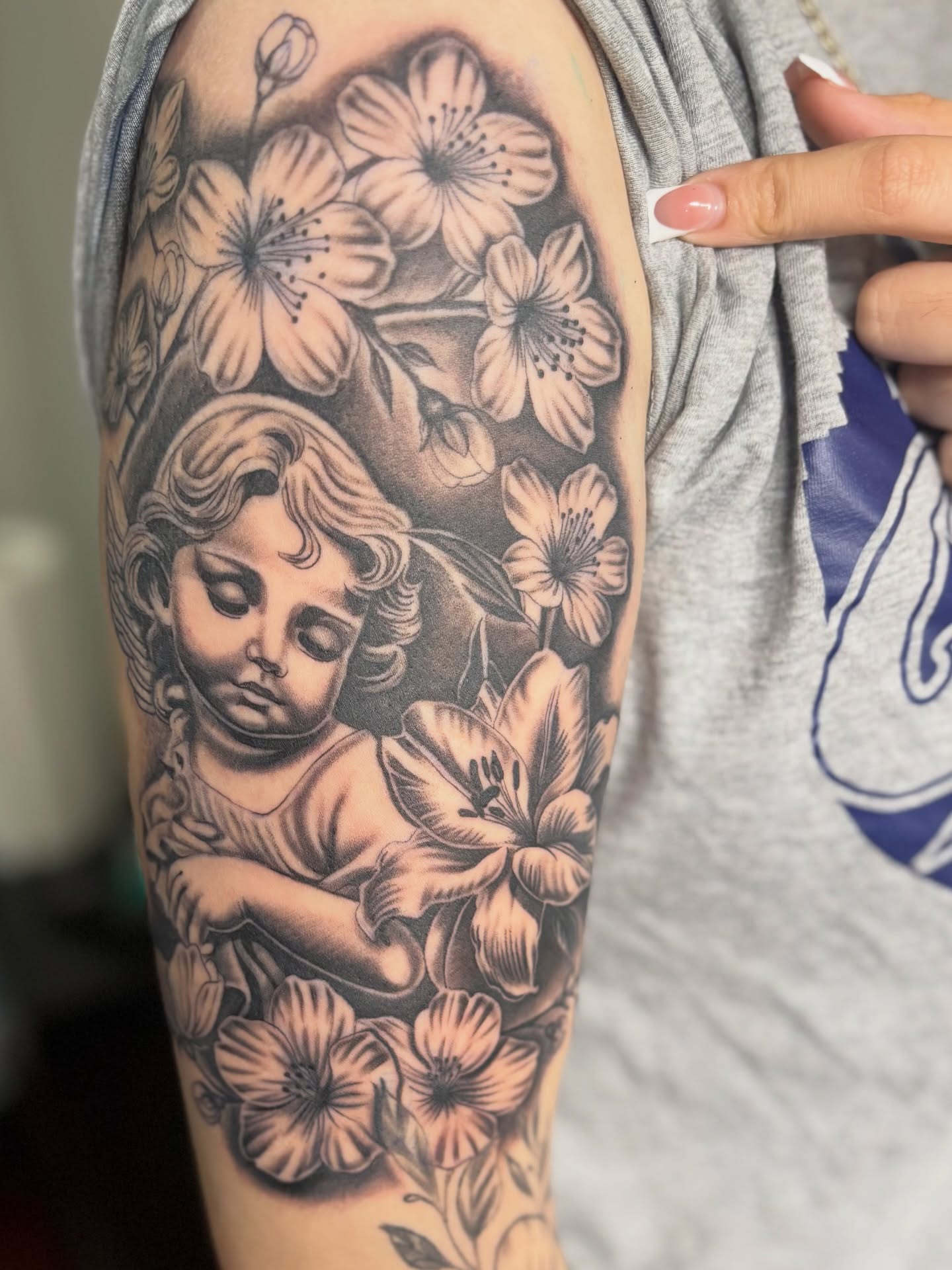 Cherub with flowers black and grey tattoo on the forearm by @tattoosbyadrian