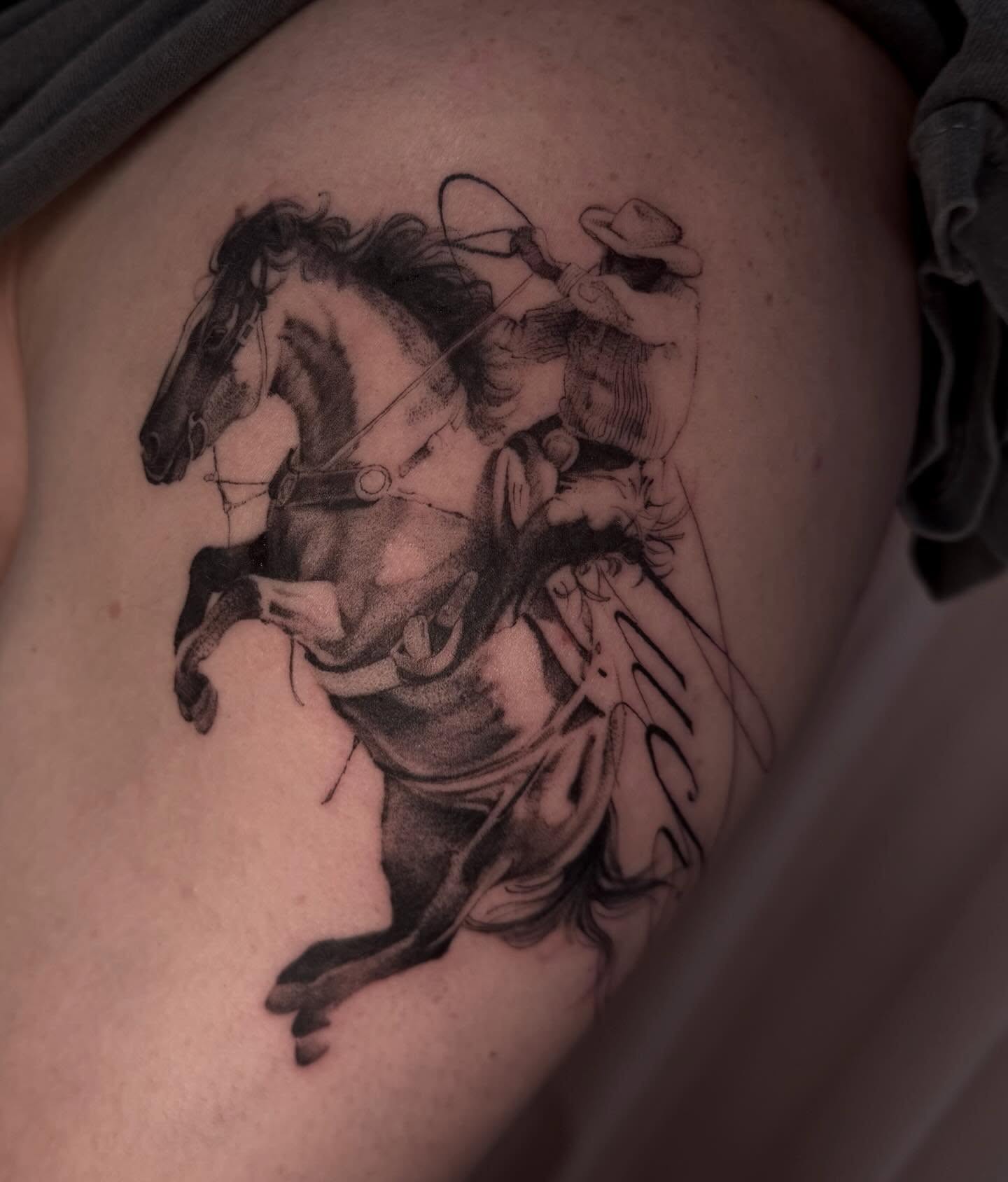 Cowboy riding horse black and grey tattoo on the thigh by Claire Litsey