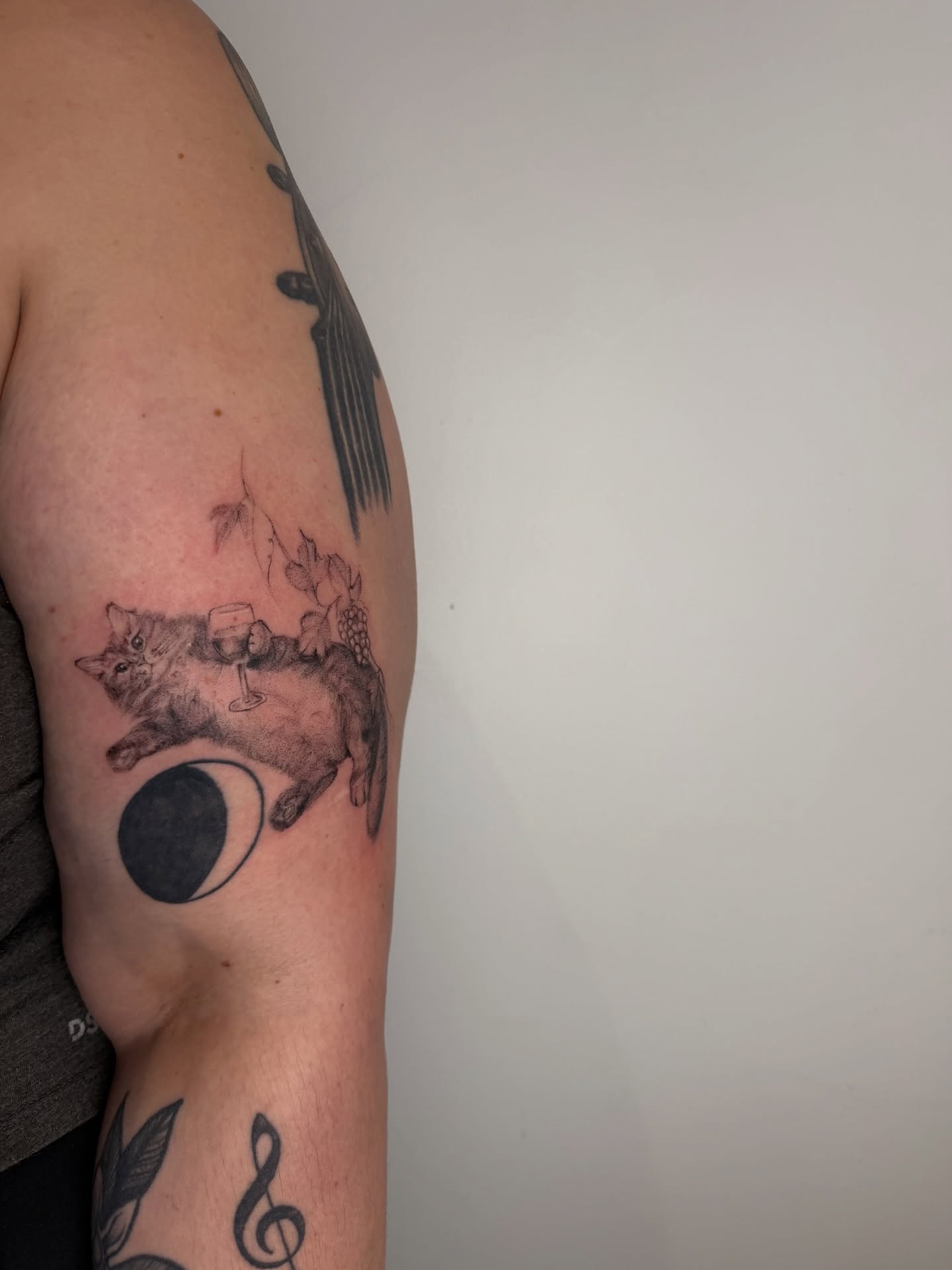 Cat with wine glass black and grey tattoo on the forearm by Mackenzie