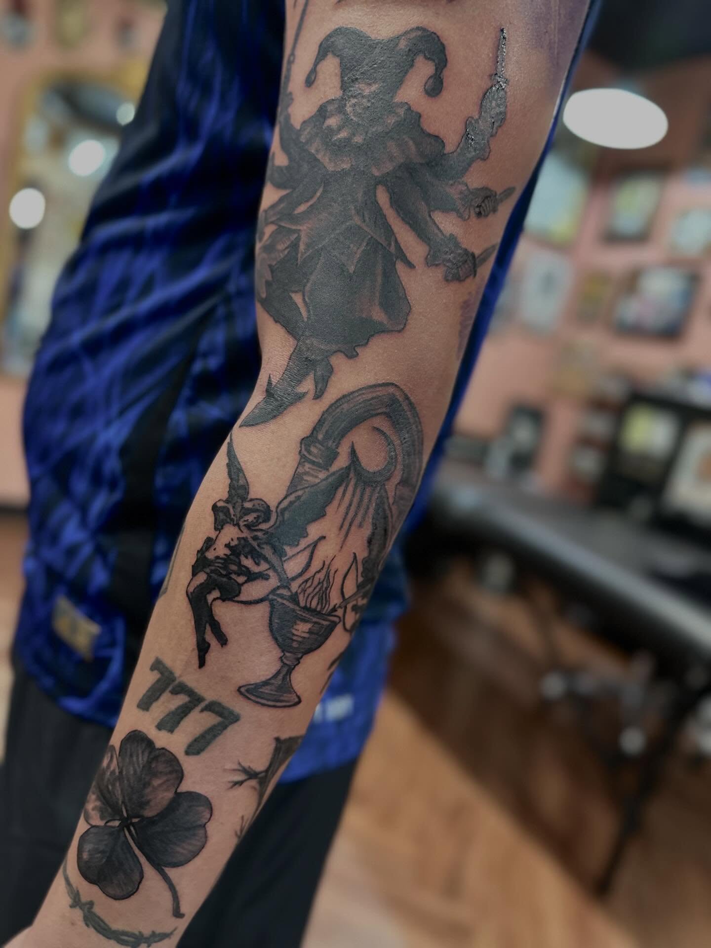 Jester and clover black and grey tattoo on the forearm by Mathilda Quynh
