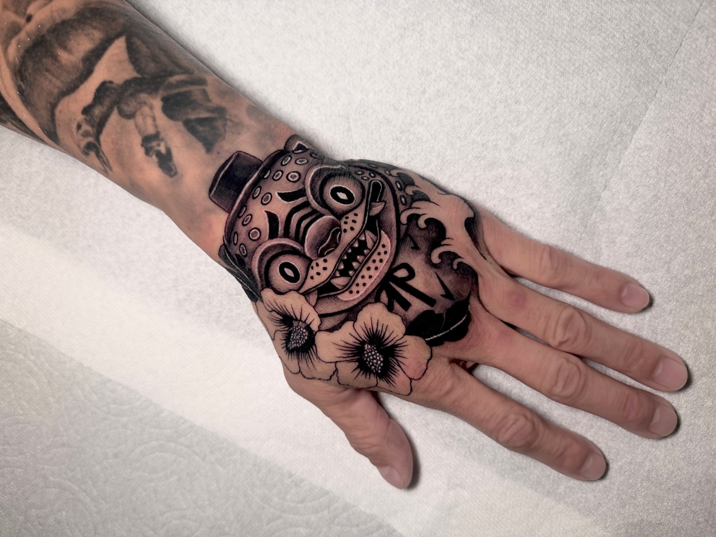Mask and flowers American traditional tattoo on the hand by LA tattoo