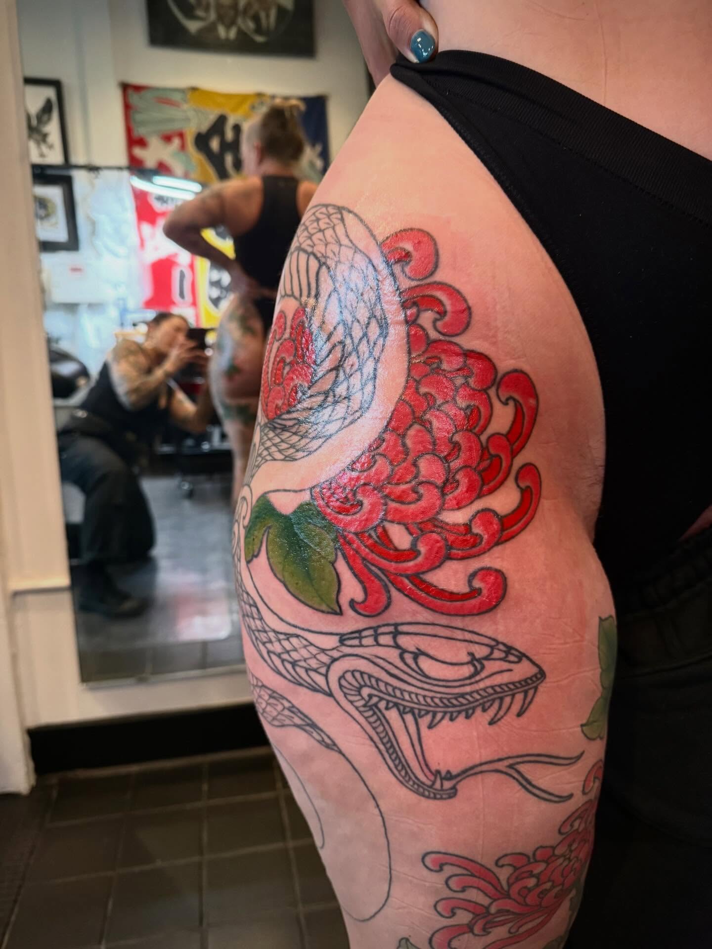 Snake and chrysanthemum American traditional tattoo on the upper arm by Candi Kinyōbi
