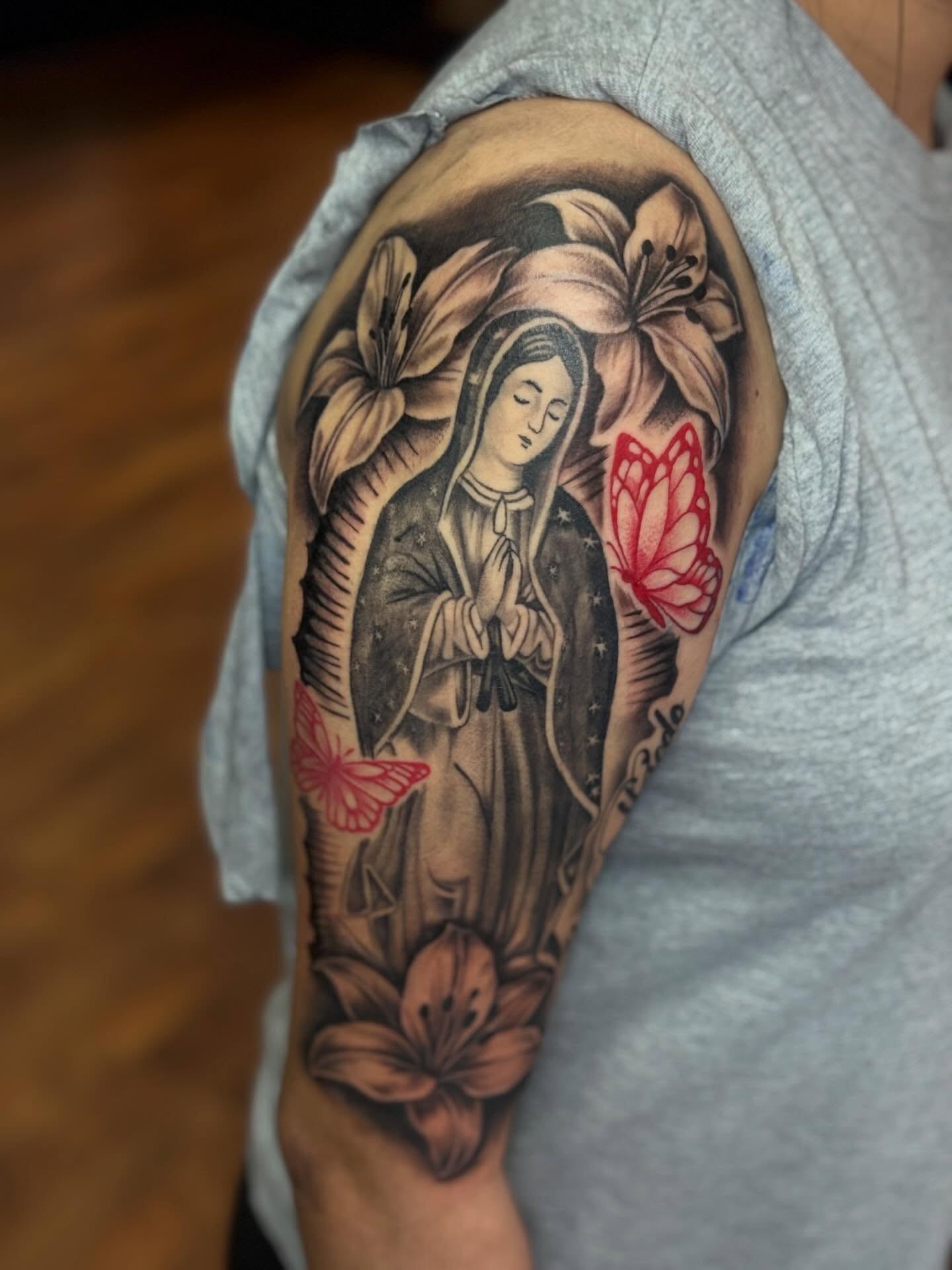Religious figure with lilies realism tattoo on the shoulder by 𓂀 𝕊ℍ𝔼𝕃𝕃𝕐 𓂀