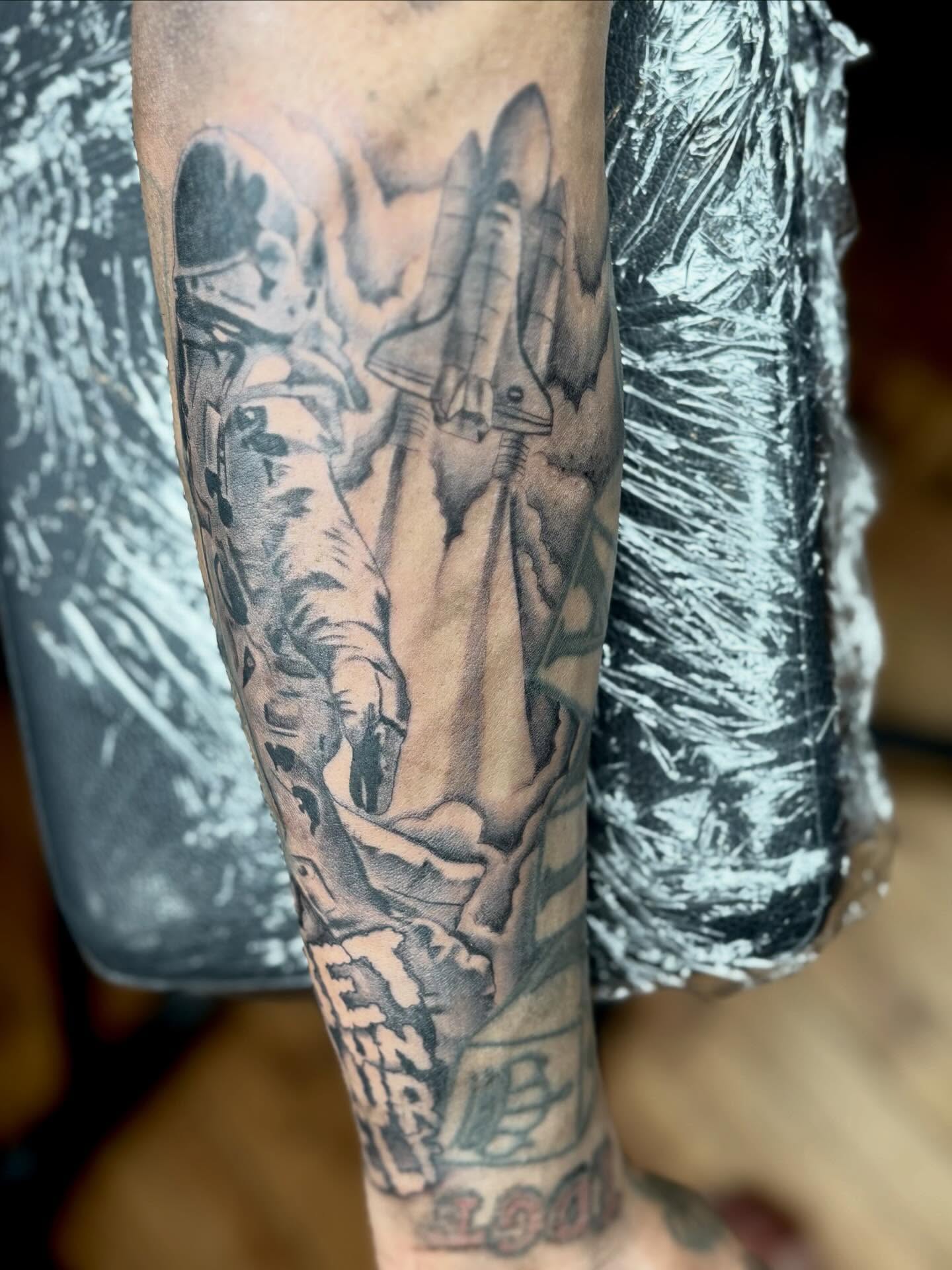 Astronaut and space shuttle black and grey tattoo on the forearm by Koolz