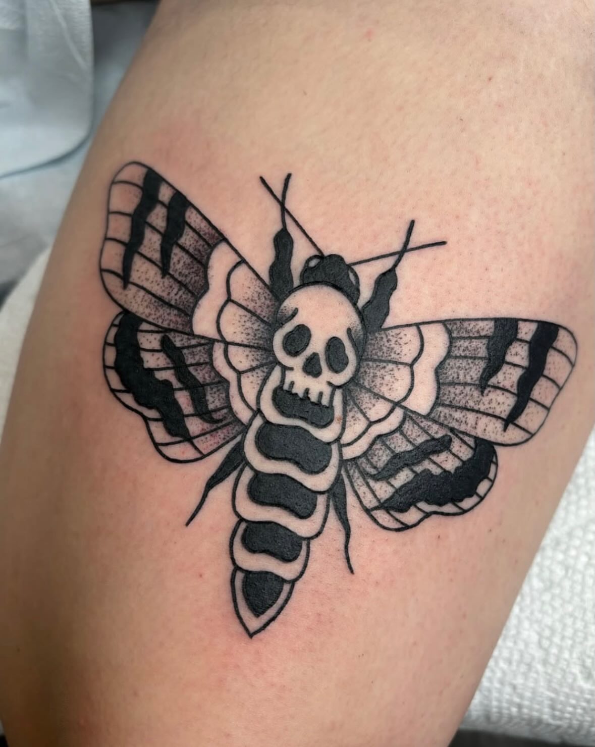 Moth with skull head dotwork tattoo on the thigh by Malia Clark