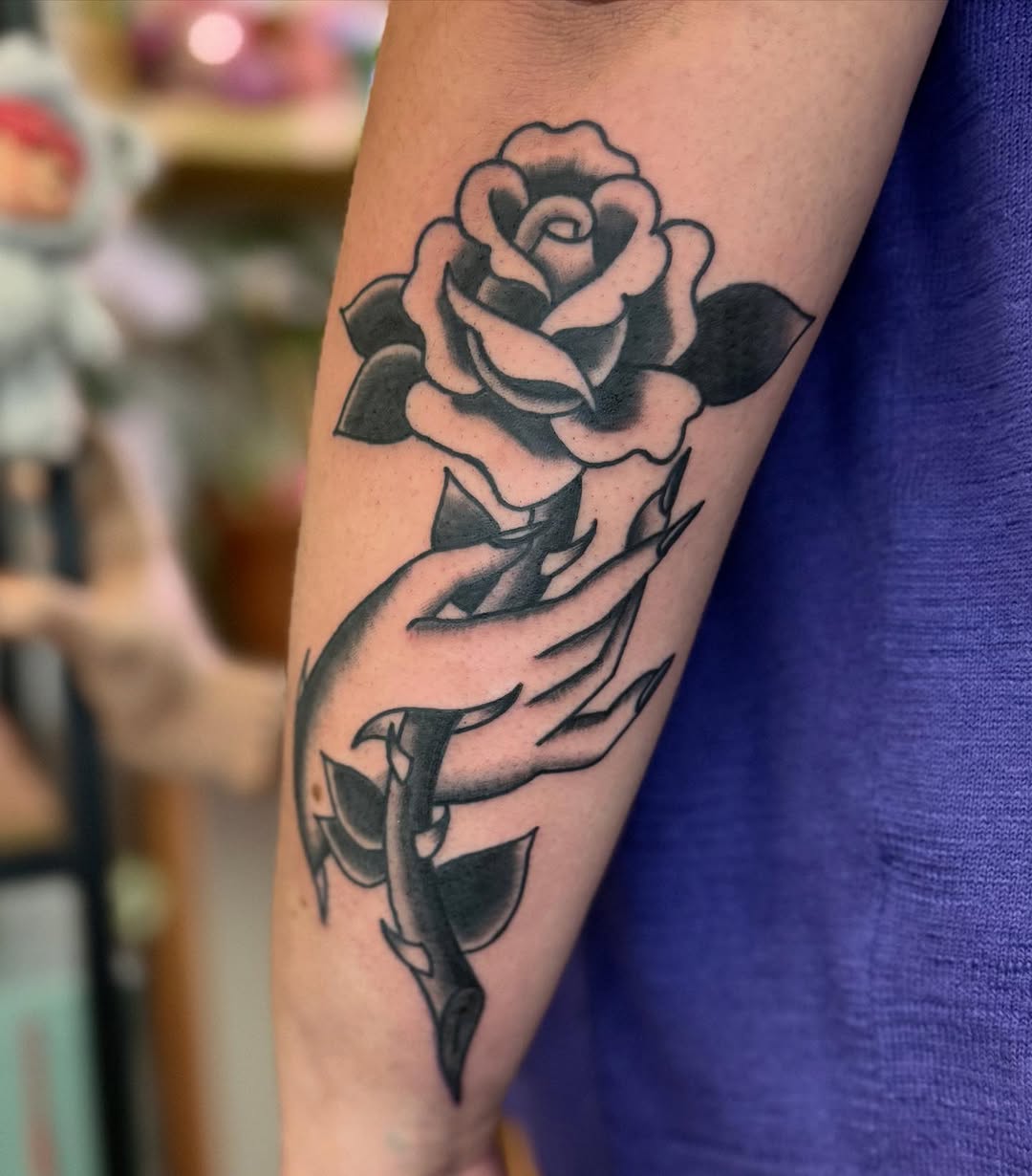 Hand holding a rose dotwork tattoo on the forearm by Rigo Vargas