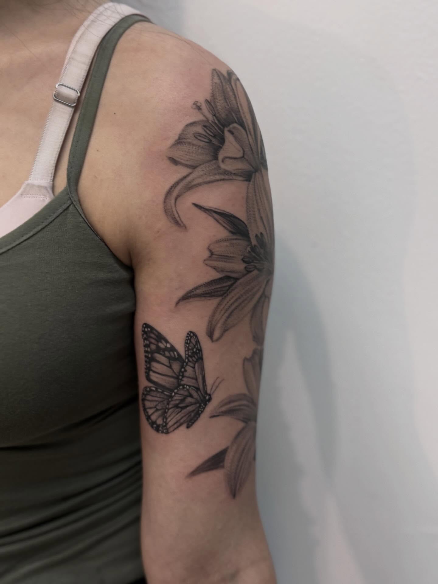 Lilies and butterfly black and grey tattoo on the upper arm by Tianna Osborne