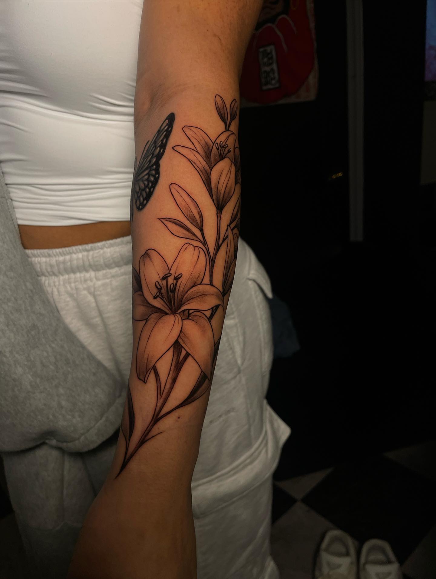 Lilies and butterfly black and grey tattoo on the forearm by Nikko