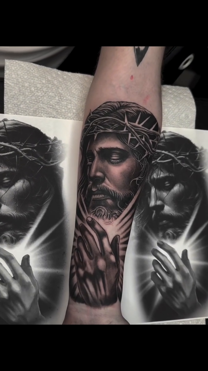 Jesus Christ portrait with praying hands Chicano tattoo on the forearm by Hugo Ruiz-Esparza