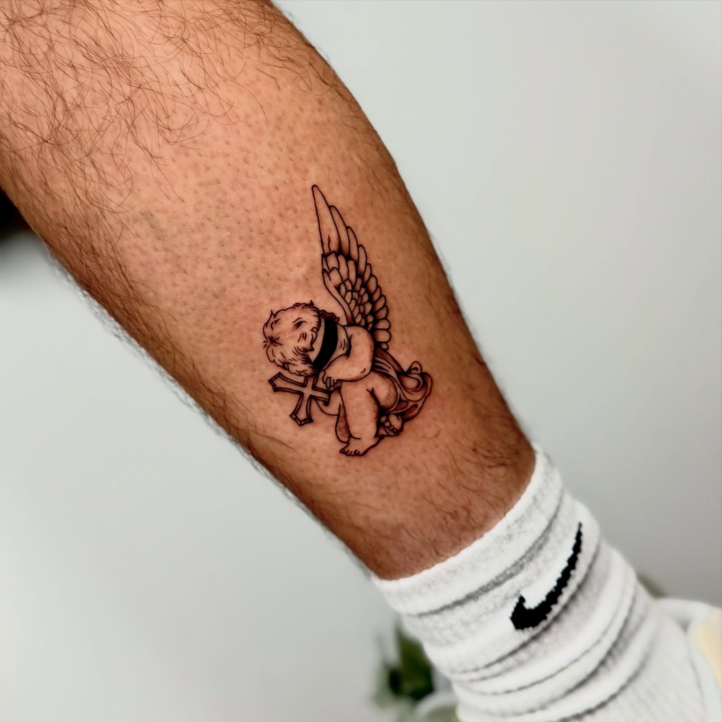Cherub with cross black and grey tattoo on the forearm by Orca