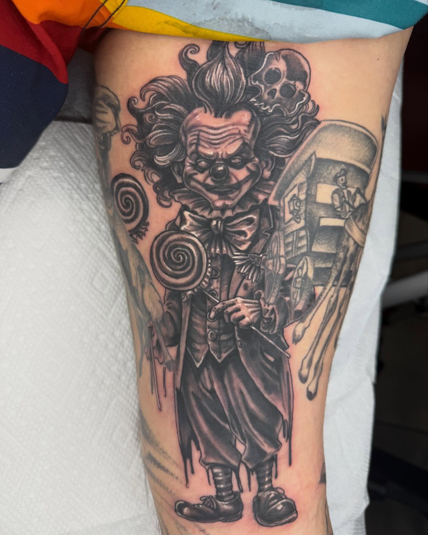 Clown with lollipop black and grey tattoo on the thigh by Frank DeMao