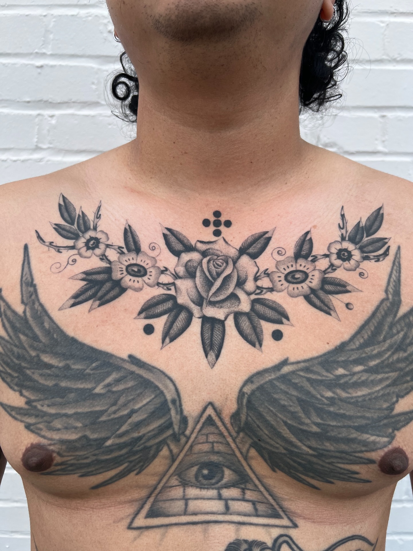 Wings and floral arrangement geometric tattoo on the chest by Cassidy Maples