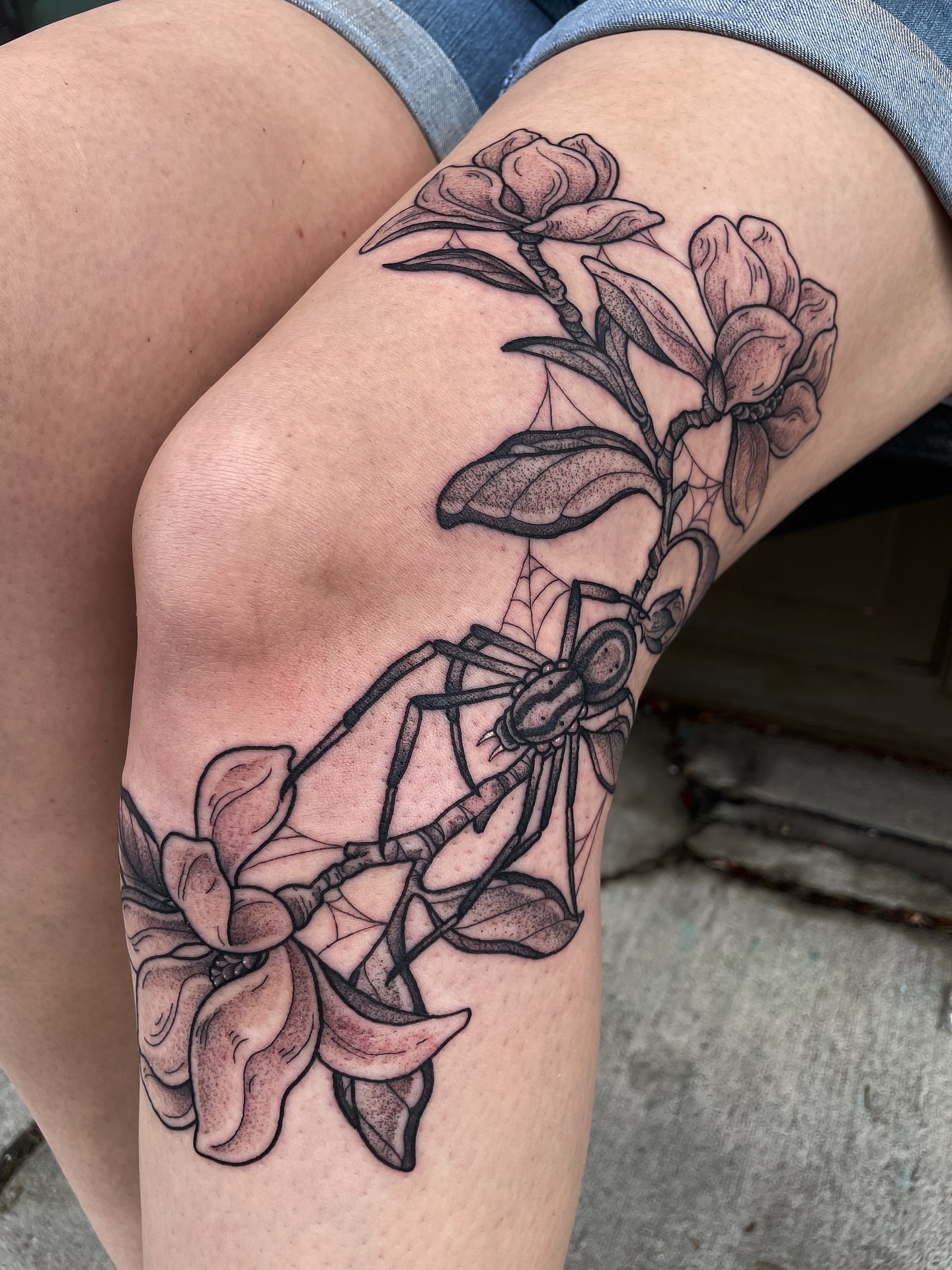 Magnolia flowers and spider realism tattoo on the thigh by Emily Lux
