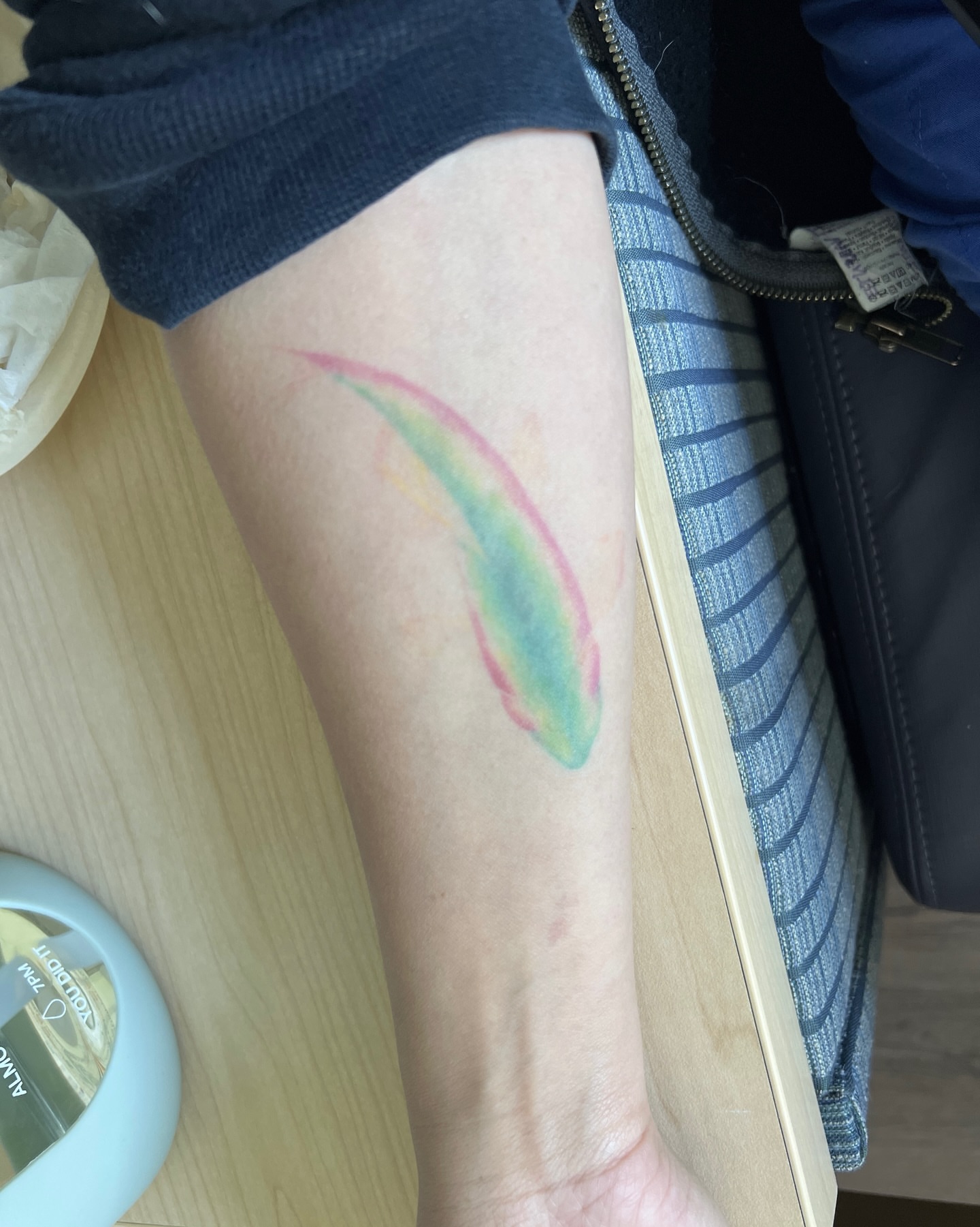 Rainbow feather watercolor tattoo on the forearm by Lea Burkard, Berkeley, California