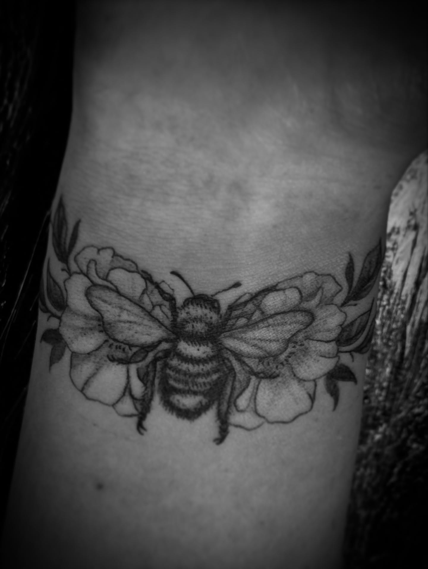 Bee and flowers black and grey tattoo on the forearm by Gianna G