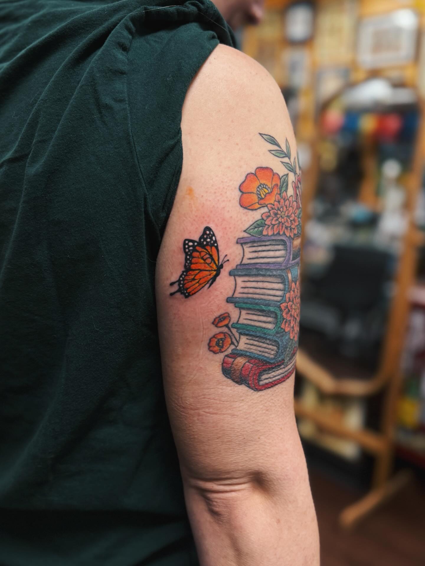 Books and butterfly watercolor tattoo on the forearm by @amandahowtattoo