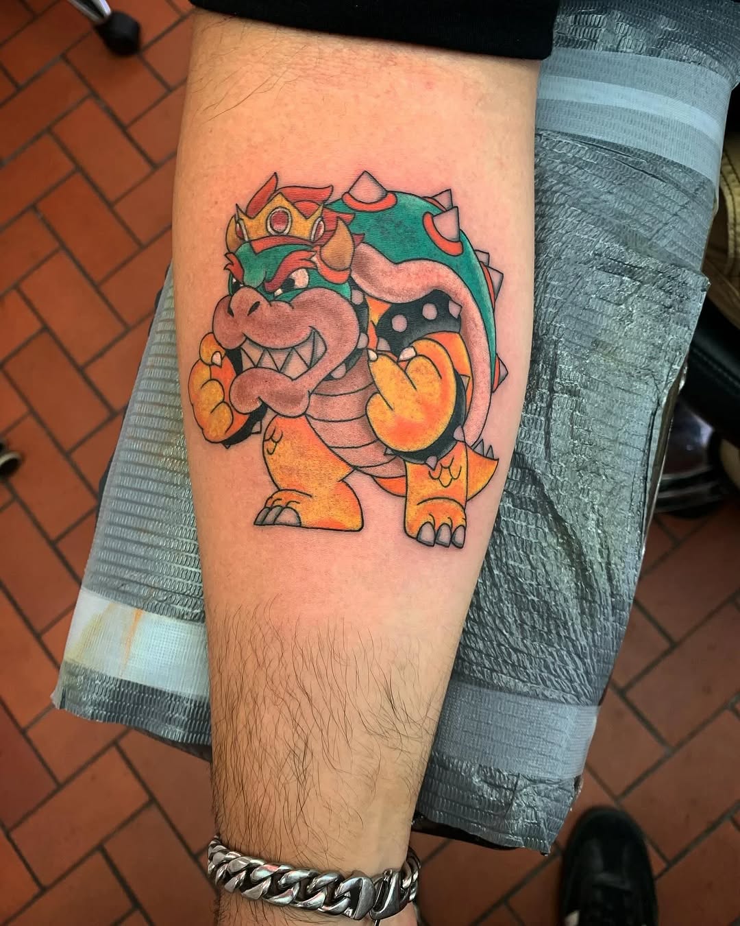 Bowser giving the middle finger new school tattoo on the forearm by Greyson Heidenreich