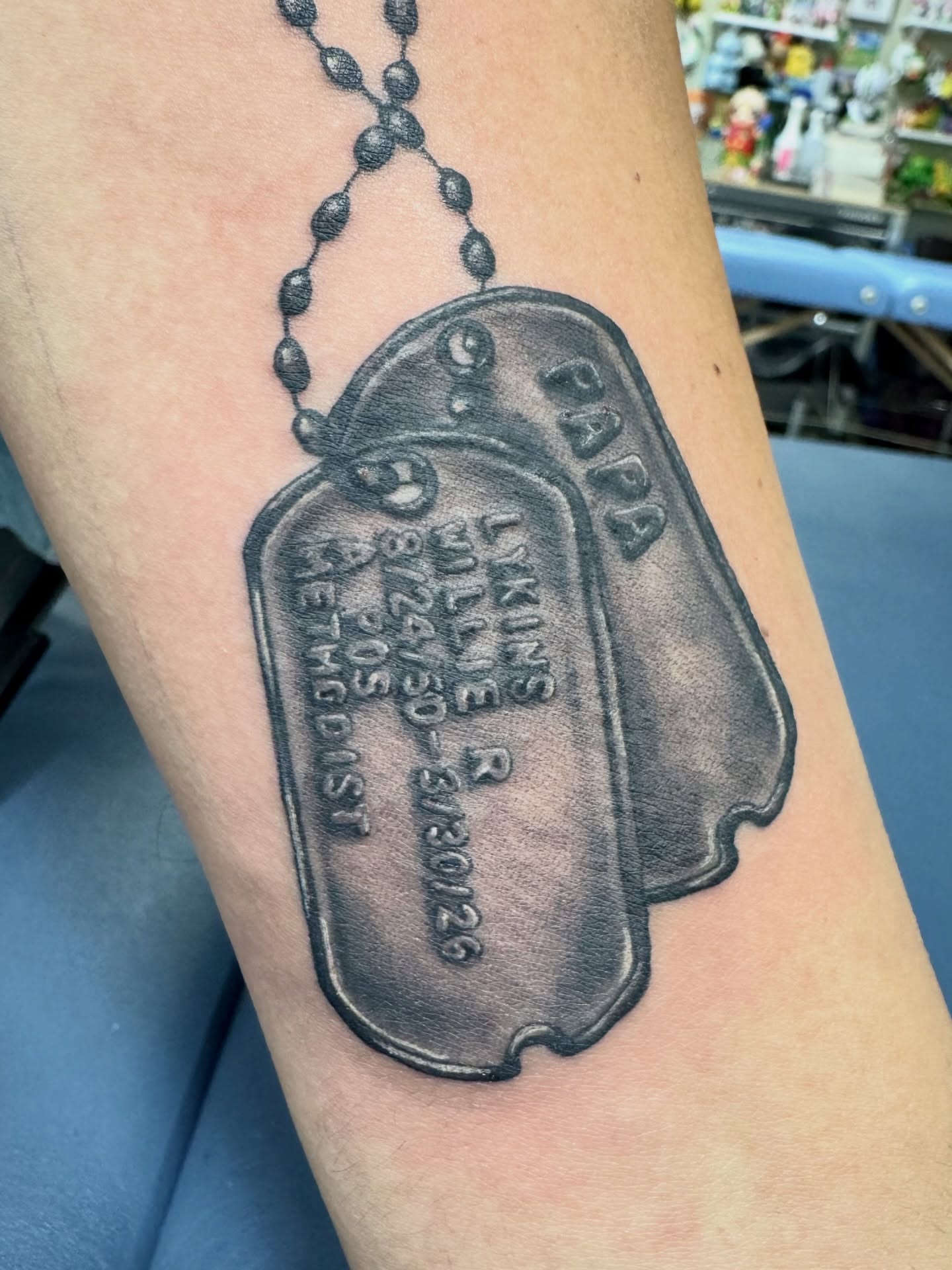 Dog tag black and grey tattoo on the forearm by Sonder