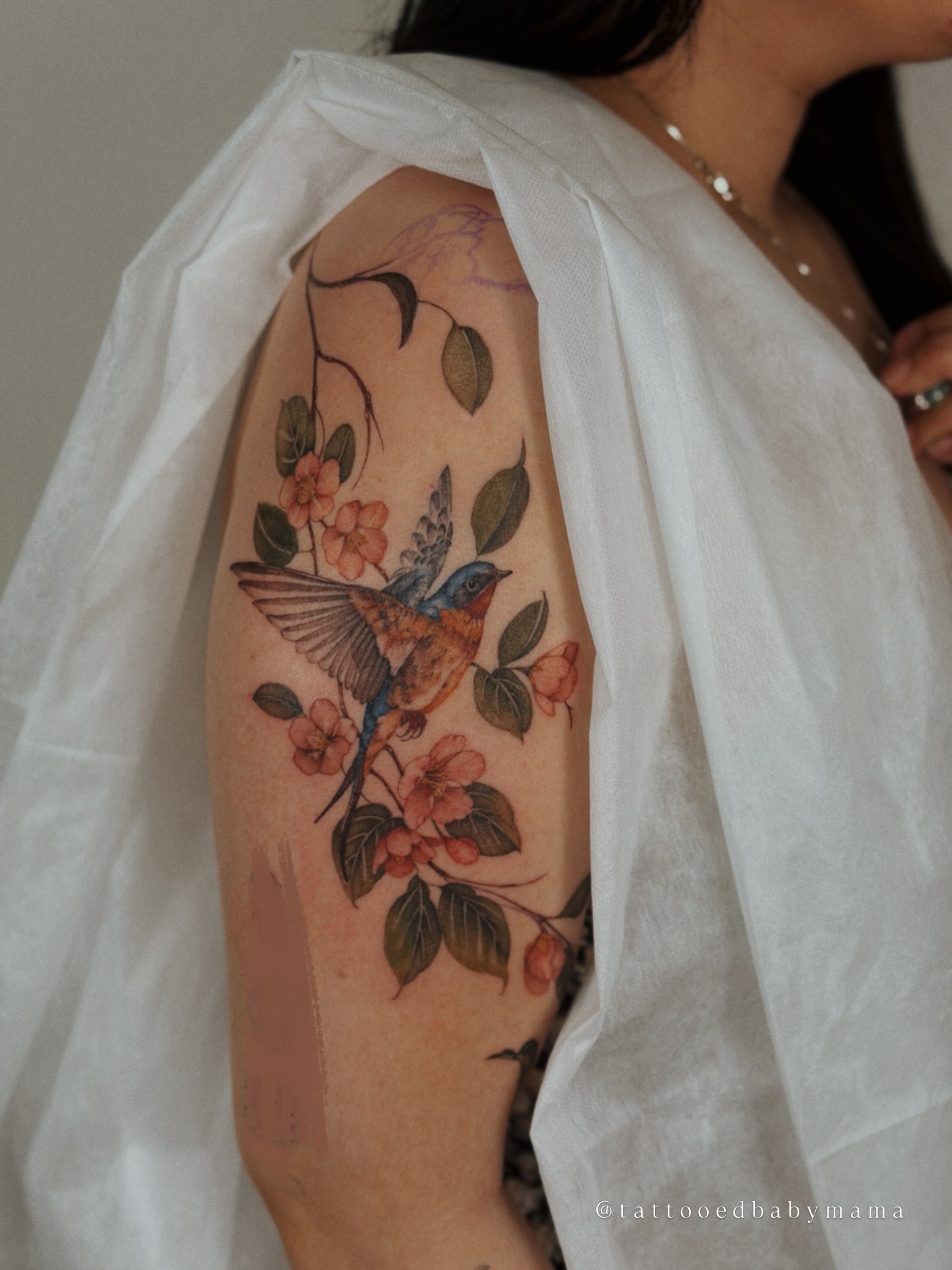 Bird and flowers realism tattoo on the upper arm by Andrea Evangelista