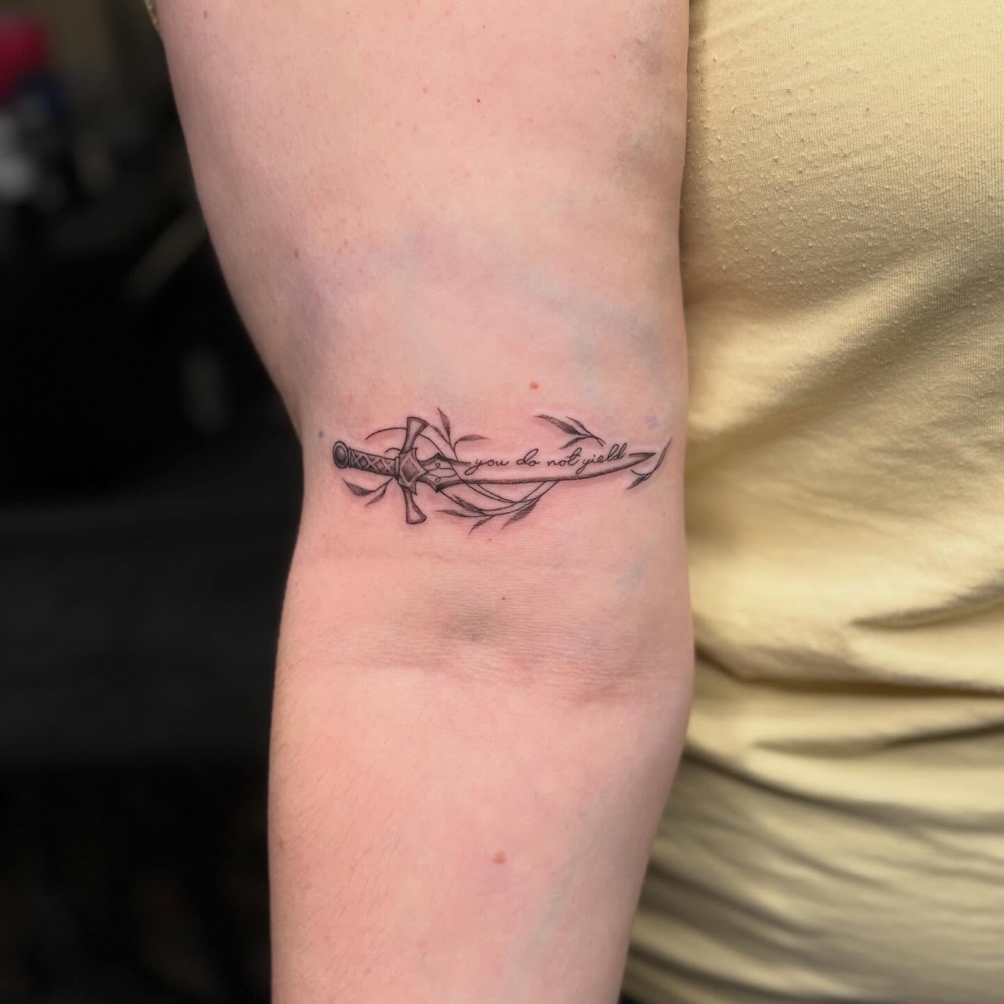 Sword and ribbon black and grey tattoo on the forearm by Tessa Simmons - Tattoo Artist