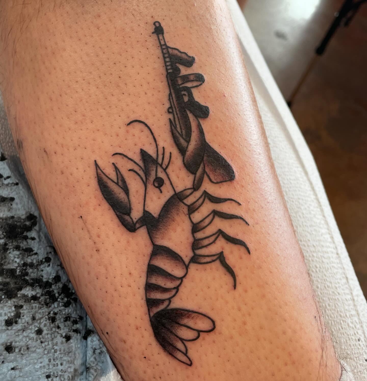 Lobster and rifle black and grey tattoo on the forearm by Lainy Lou