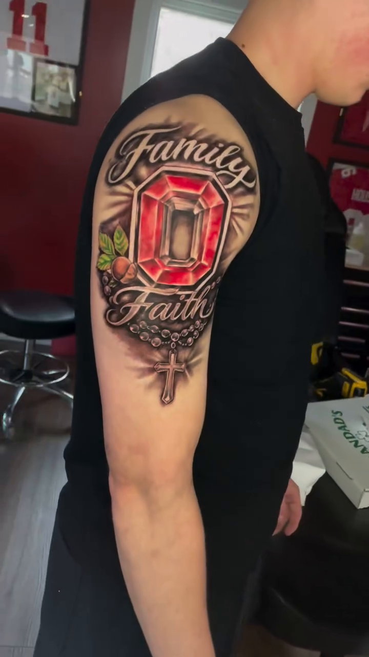 Gemstone with "Family" and "Faith" text Chicano tattoo on the upper arm by Inkman Parson