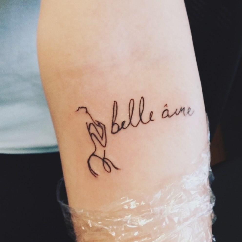 Figure and script lettering tattoo on the forearm by Amber