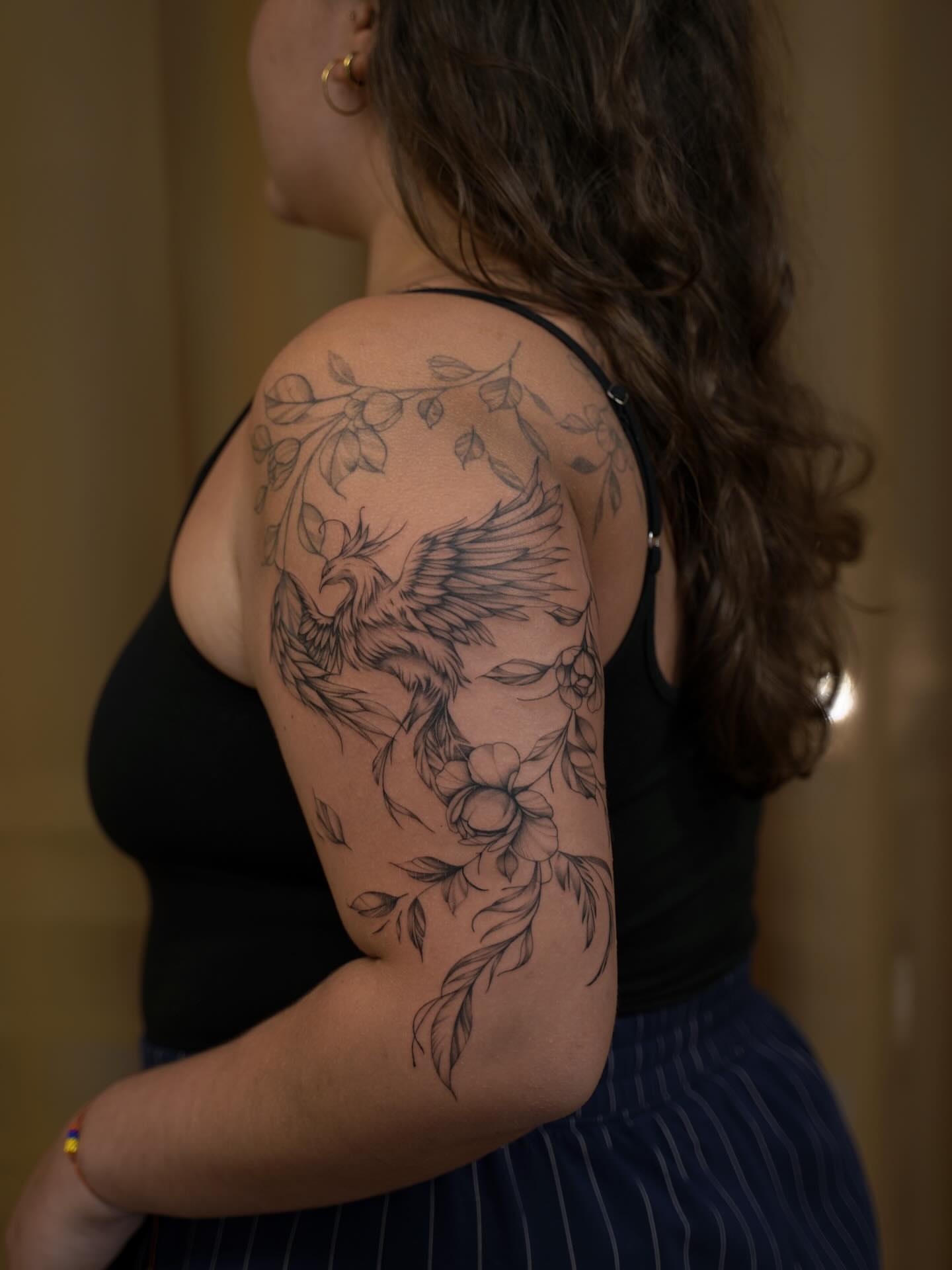 Phoenix and floral black and grey tattoo on the upper arm by Christian Guerrero